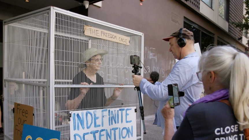 Sister Brigid Arthur an activist nun, standing inside a metal cage being interviewed by journalists