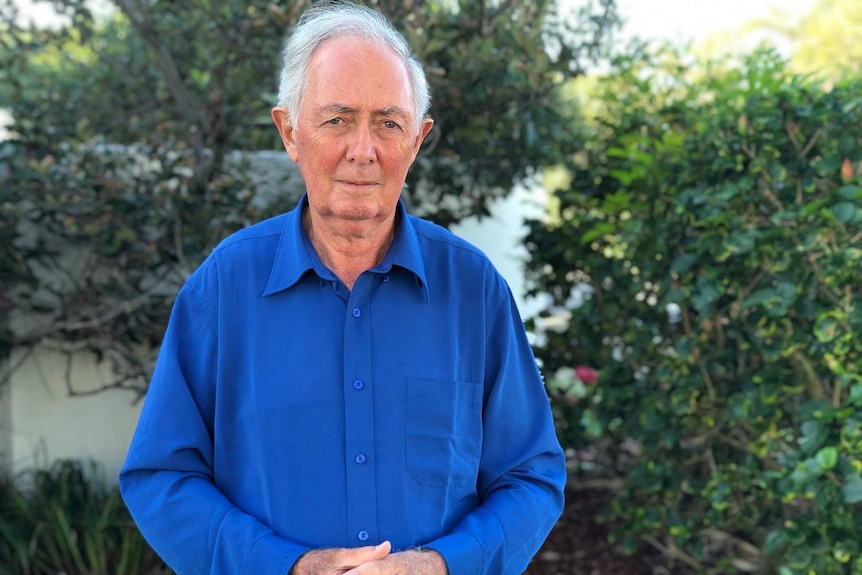 Professor Ian Lowe stands with his hands clasped in front of his body.