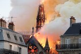 The roof and spire of a gothic cathedral are burned by bright orange flames while thick smoke fills the sky