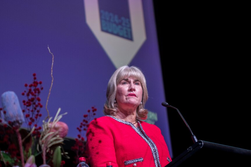 a blonde woman wearing a hot pink blazer speaking at a lectern