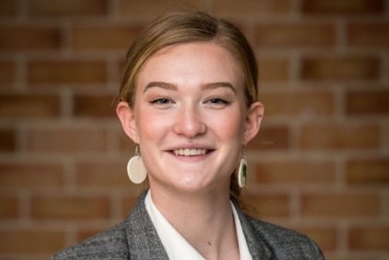 A woman smiles in front of a brick wall.