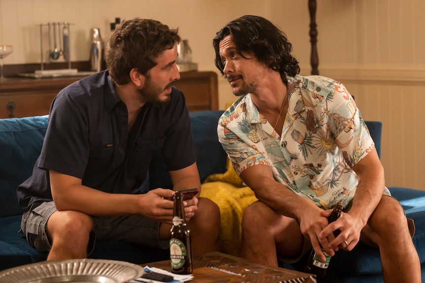 Two actors sitting down in discussion, a beer on the table in front of them. They're looking at each other.