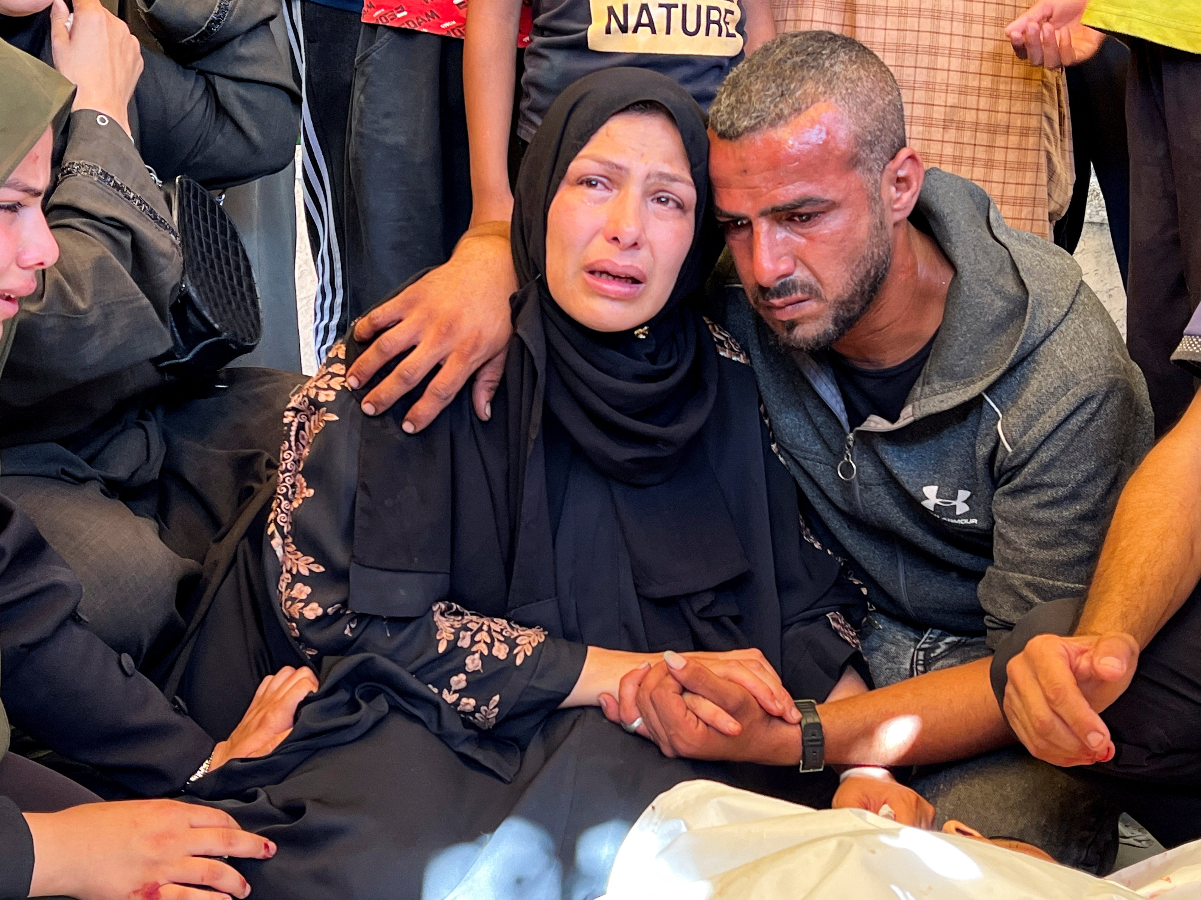 A man in a grey hoodie looking distressed sitting alongside a woman crying in a dark headdress