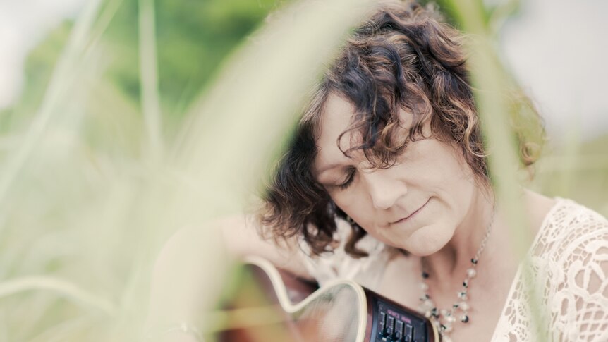 woman holding guitar in long grass