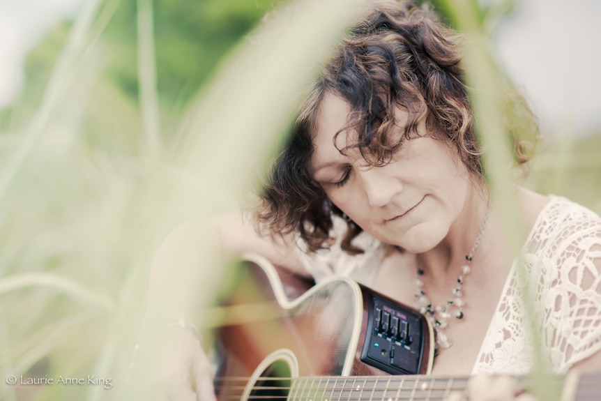 woman holding guitar in long grass