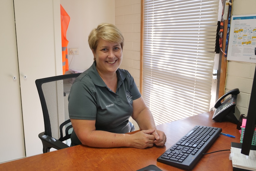 A woman sitting at a desk in an office, smiling at the camera