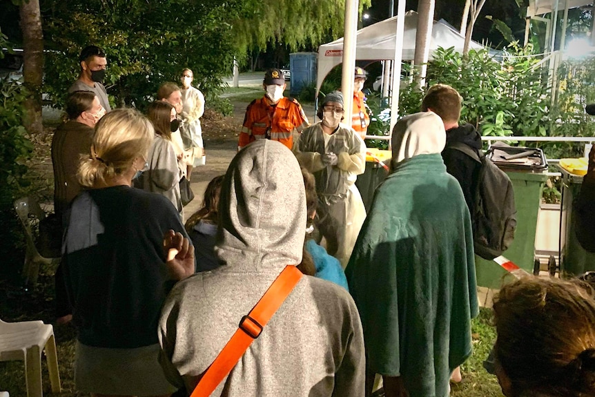 Crowd of people listen to a nurse in personal protective equipment, at night on Magnetic Island