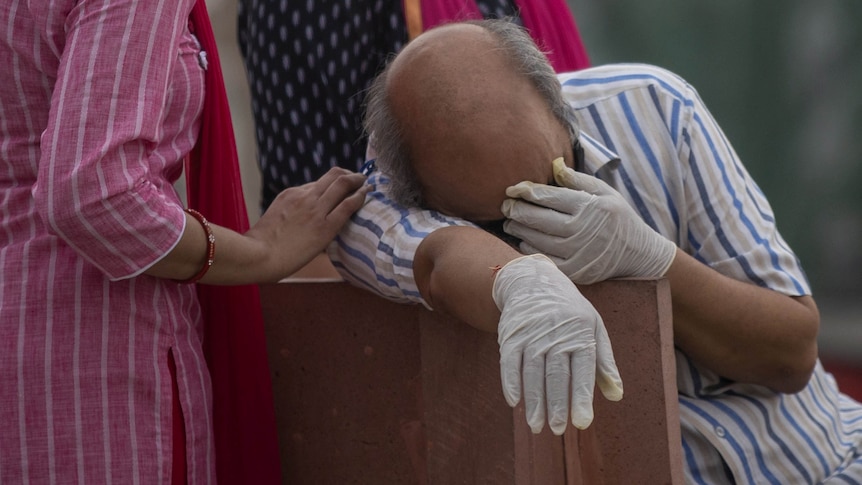 Un uomo indiano piange nella mano sinistra prima della cremazione di un membro della famiglia morto per COVID-19.