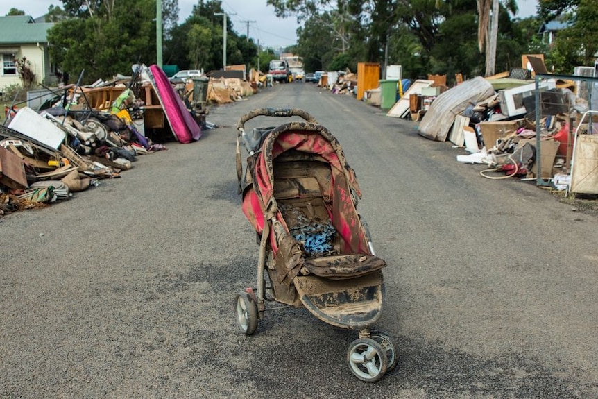 A dirty pram stands in the middle of the road. The sides of the road have piles of rubbish down them.