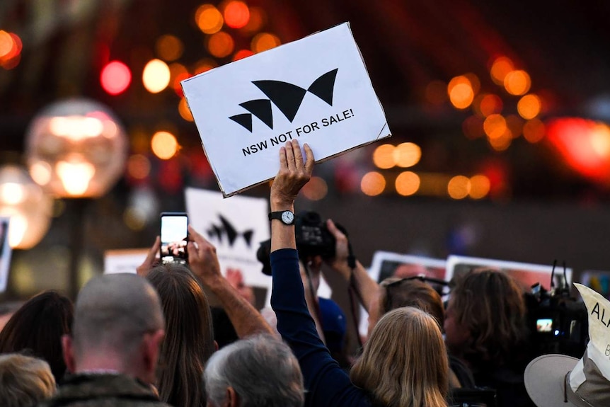 A hand holding a sign that reads "NSW not for sale"