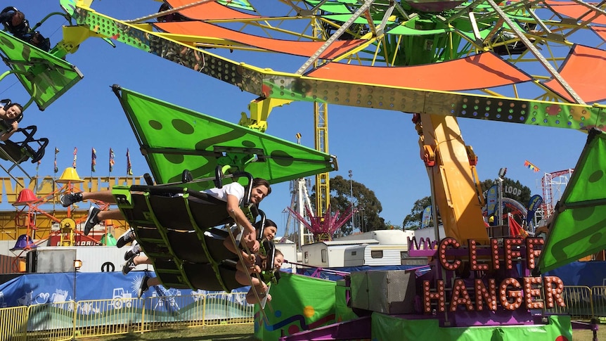 People lying on the cliff hanger green and orange ride at an agricultural show.