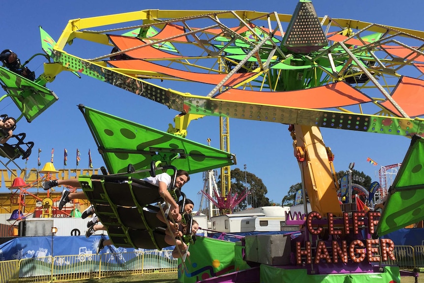 People lying on the cliff hanger green and orange ride at an agricultural show.