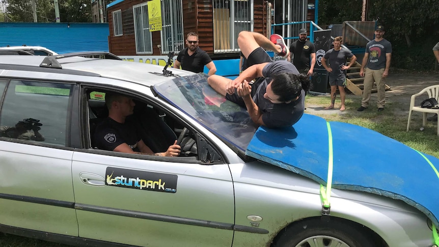 A man rolls on the bonnet of a car