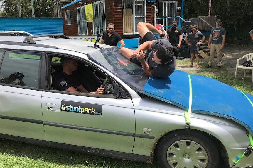 A man rolls on the bonnet of a car