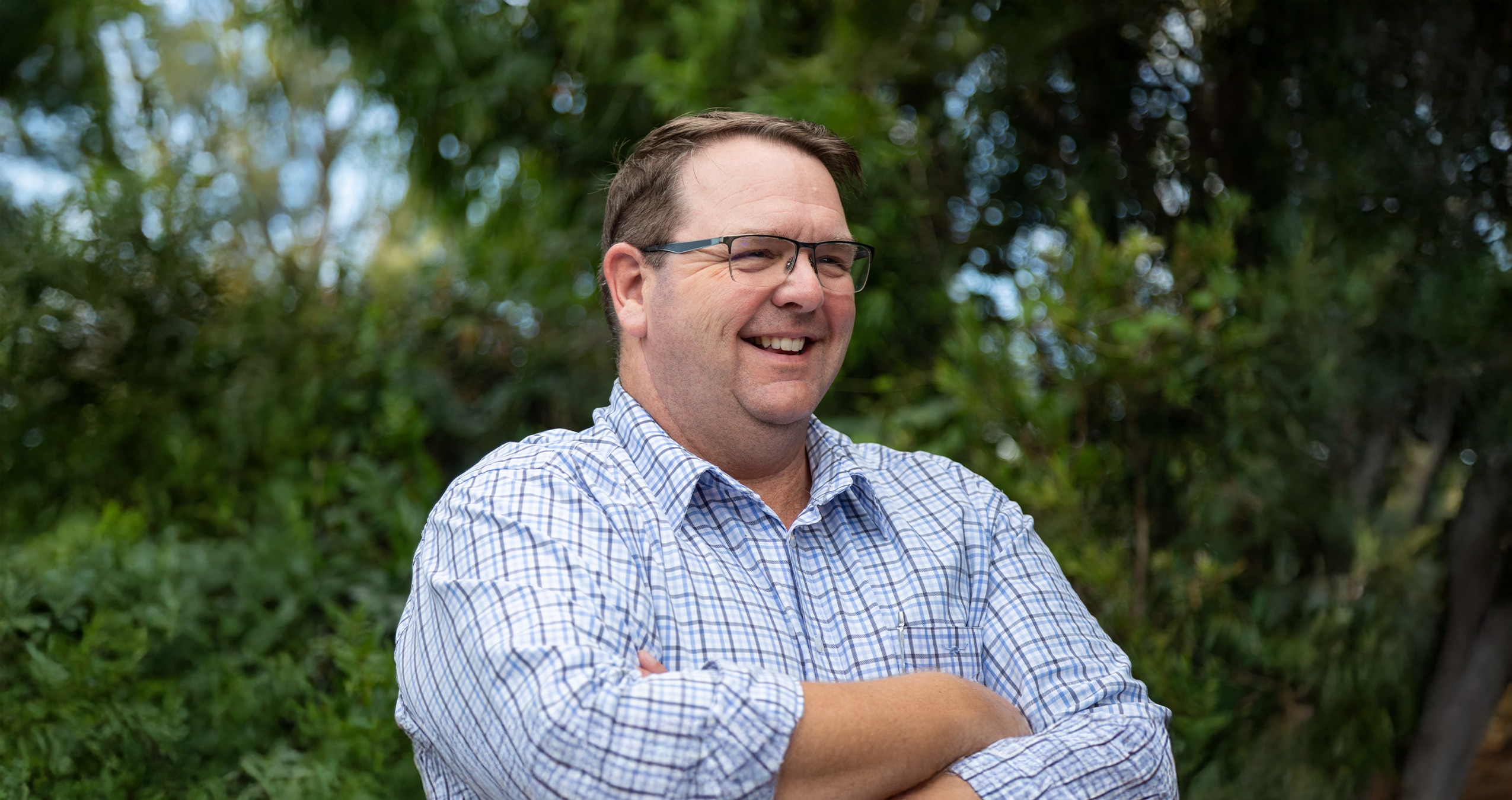 um homem com uma camisa xadrez sorrindo e cruzando os braços