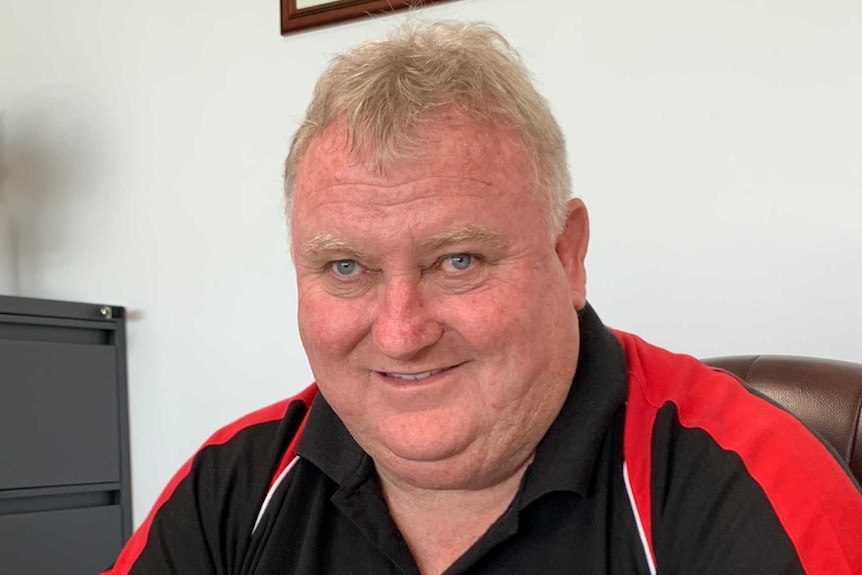 A man wearing a black and red polo shirt sits at a desk in an office