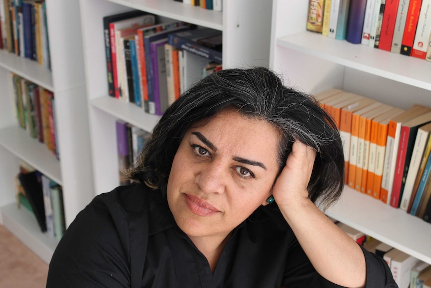 Iranian-Australian writer Shokoofeh Azar resting on her hand, bookcase in the background