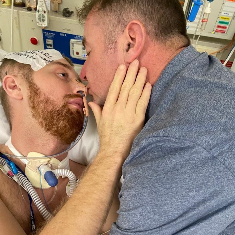 Danny Hodgson's father leans in to give his son a kiss while he is lying in a hospital bed.