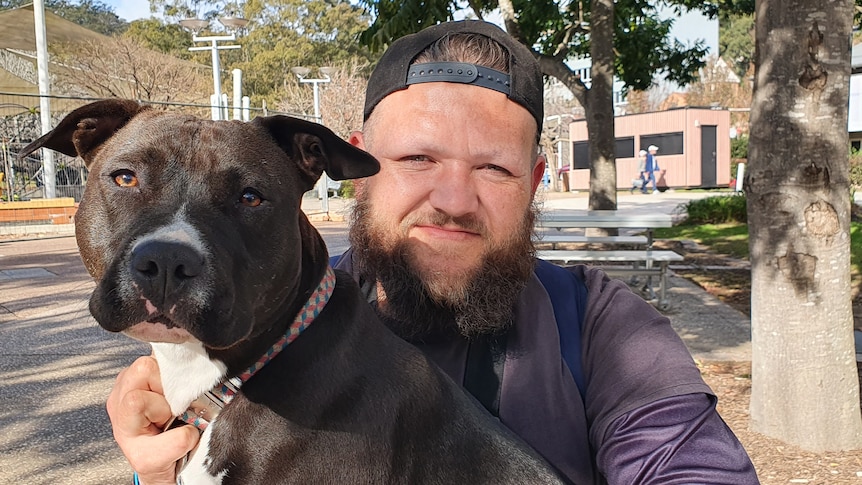 Jason Trindall-Rynkowsi, Kamilaroi man and HotS client sits with his brown dog. Gosford 2022