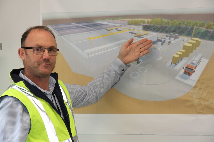 A man stands in front of plans mounted on a whiteboard