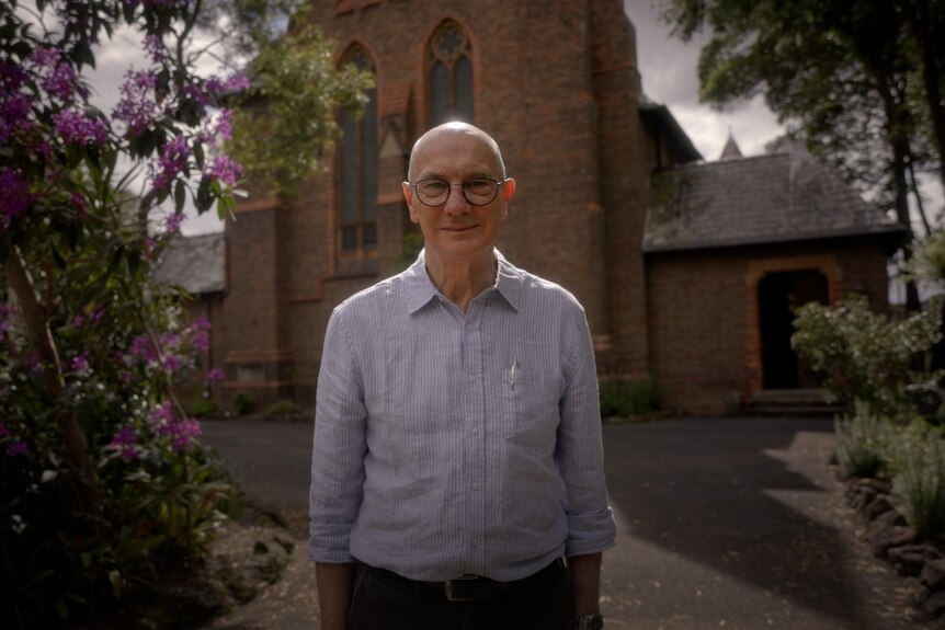 A middle-aged bald man stands in front of a church