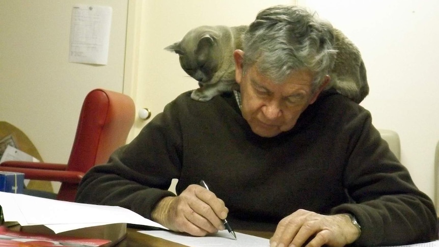 The Reverend Tony Lang studying with cat sitting on shoulder.