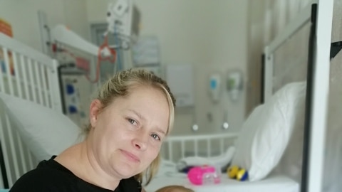 A mother holds her bandaged 10-month-old baby in a hospital room.