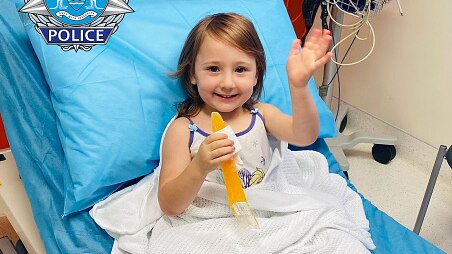 A little girl waves from a hospital bed