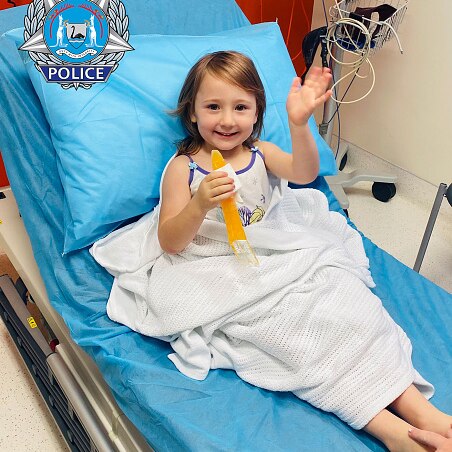 A little girl waves from a hospital bed