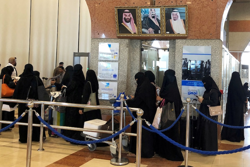 A number of woman in black burkas bustle around a ticket window