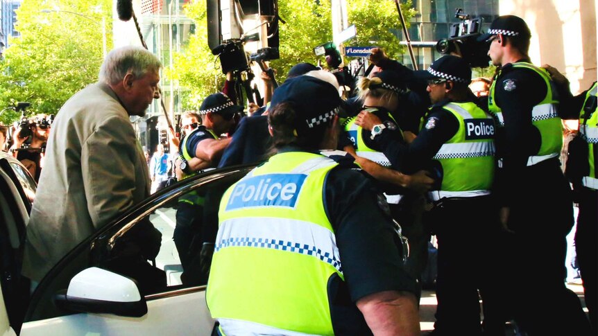 Cardinal George Pell steps out of a car with a police escort after arriving at the Melbourne Magistrates' Court.