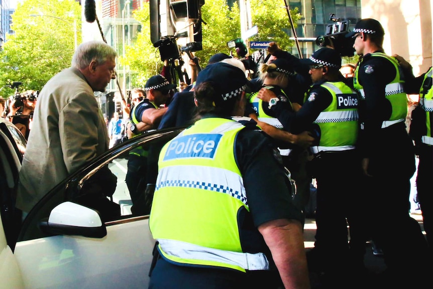 Cardinal George Pell steps out of a car with a police escort after arriving at the Melbourne Magistrates' Court.