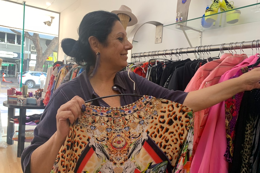 A woman with dark hair smiles as she puts a dress on a rack in a shop