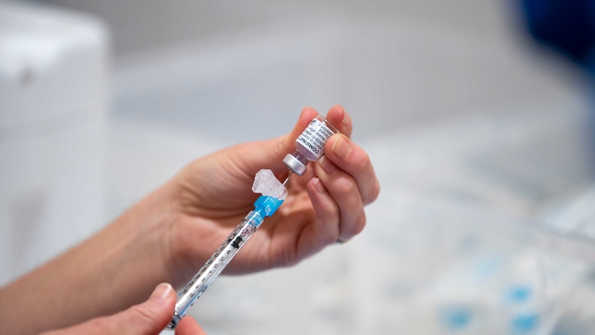A person inserts a needle into a dose of Pfizer vaccine.
