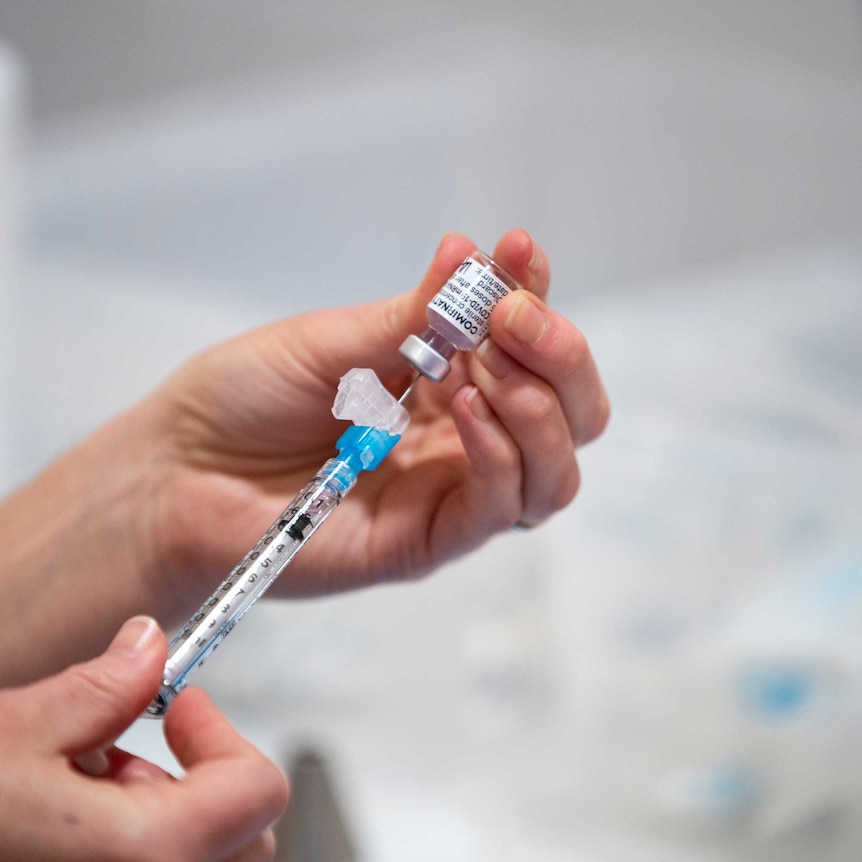 A person inserts a needle into a dose of Pfizer vaccine.