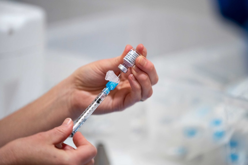 A healthcare worker holds a viral of COVID-19 vaccine and draws up a needle.