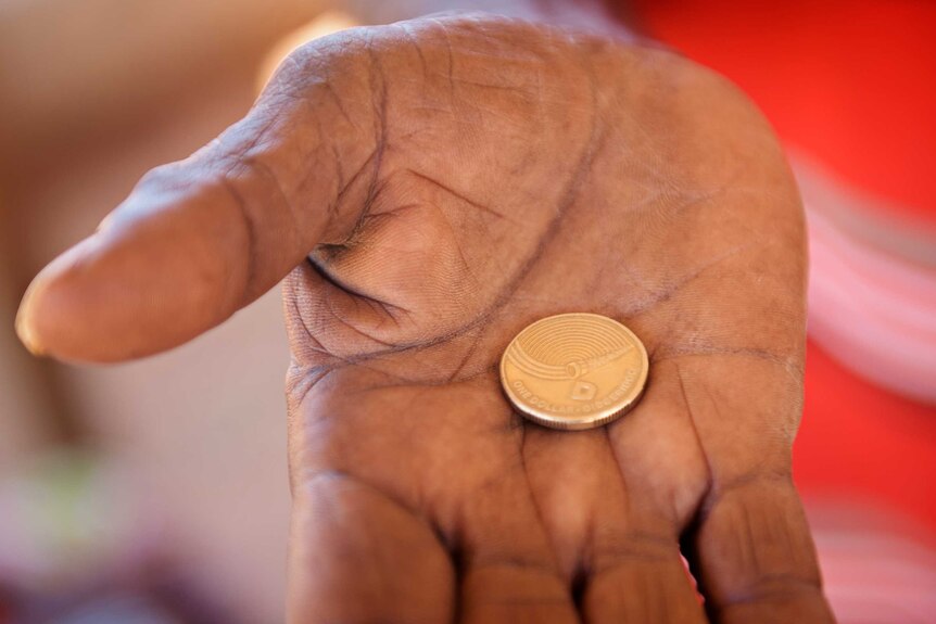 A hand holds a new dollar coin last year featuring the design of Djalu Gurruwiwi.