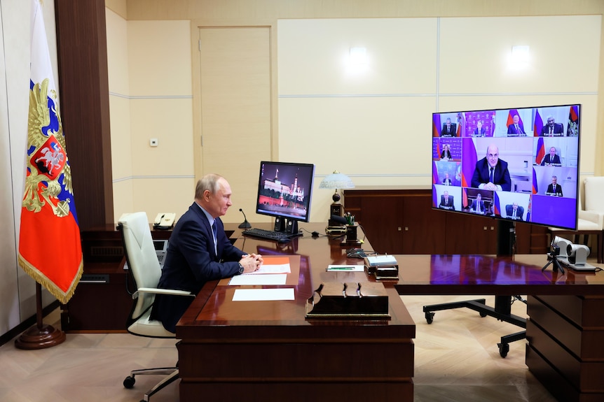 Vladimir Putin at a large desk, talking to members of the Security Council on a large screen.