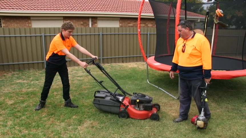 Brodie Lunn mowing lawn with support worker Kerry Wilson