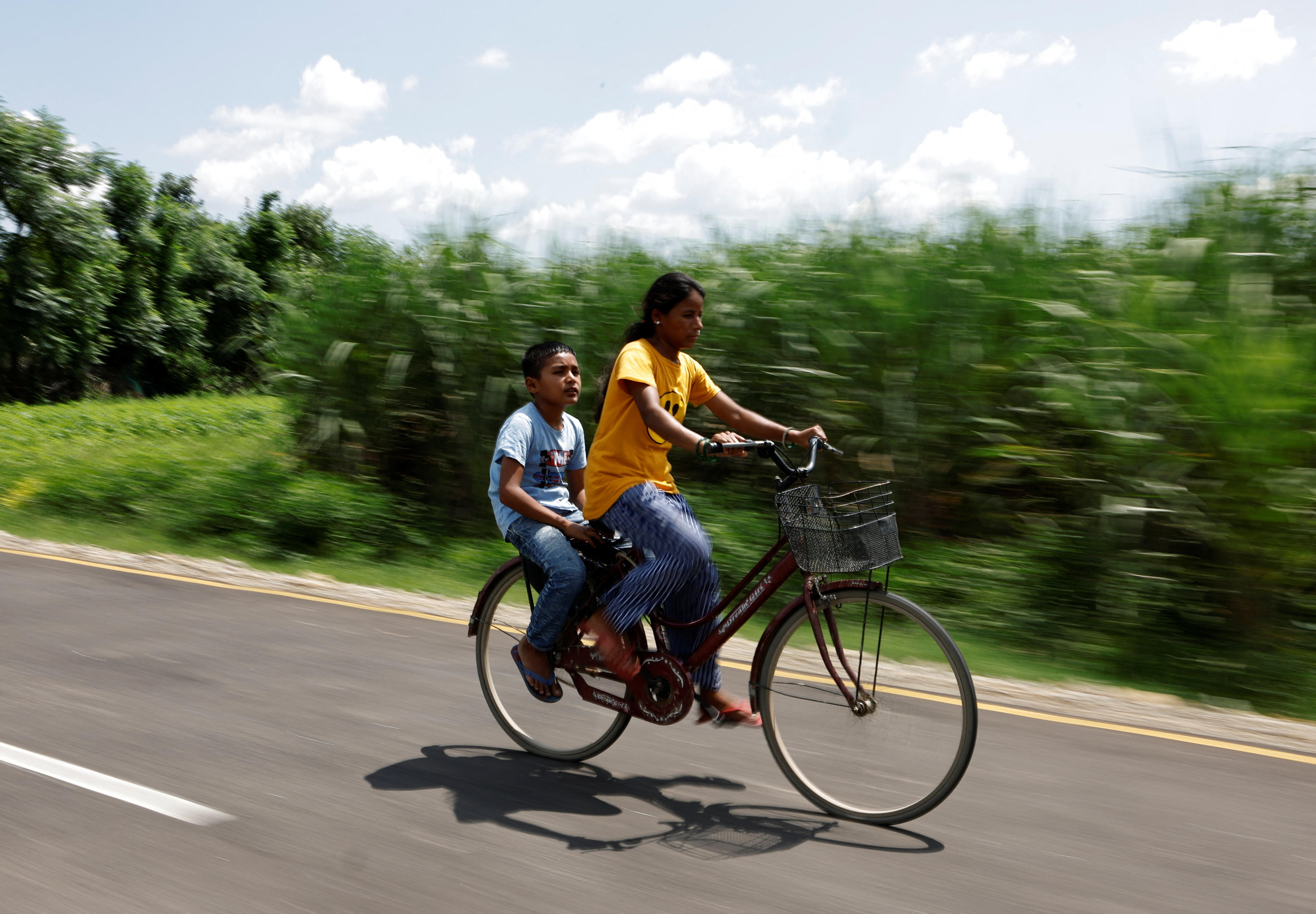 A woman and a young boy ride on a bicycle on a road as fields rush past them