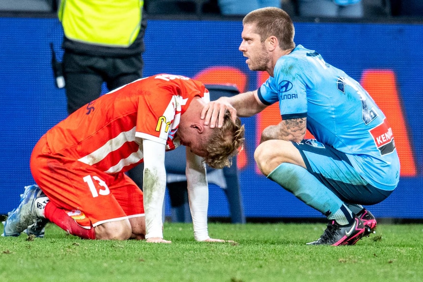 Luke Brattan kneels down in front of Nathaniel Atkinson, who is on his knees