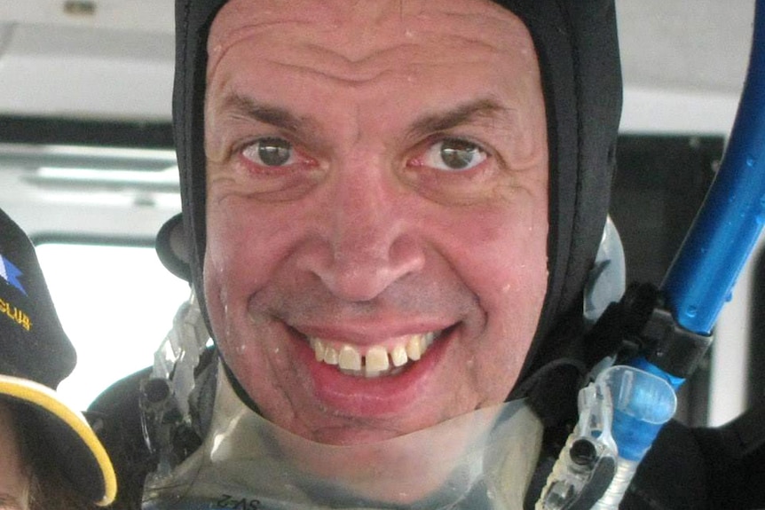 A close-up shot of a smiling man wearing scuba diving goggles, a snorkel and a wetsuit.
