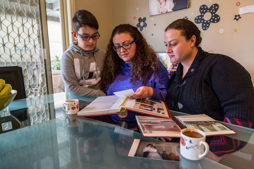 Sonia Sofianopoulos' grandson Adam and daughters Eleni Kontogiorgis and Stella Sofianopoulos look through photo albums a table