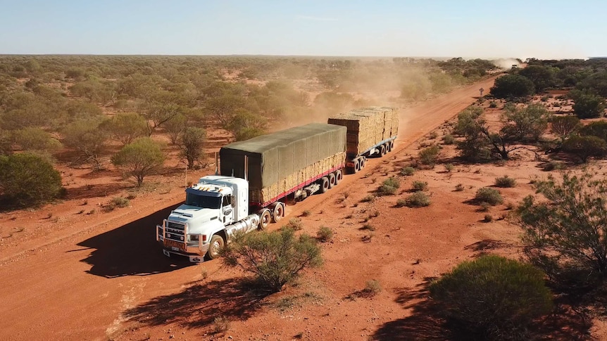 A convoy of trucks drive along a dusty road