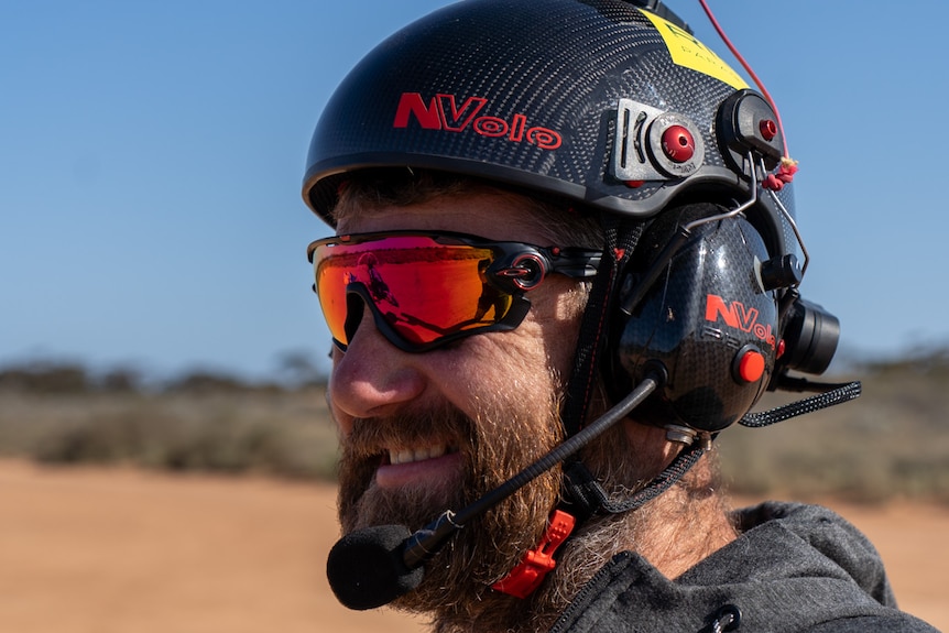 An adventurous-looking man with red reflective sunglasses and a helmet smiles into the distance.