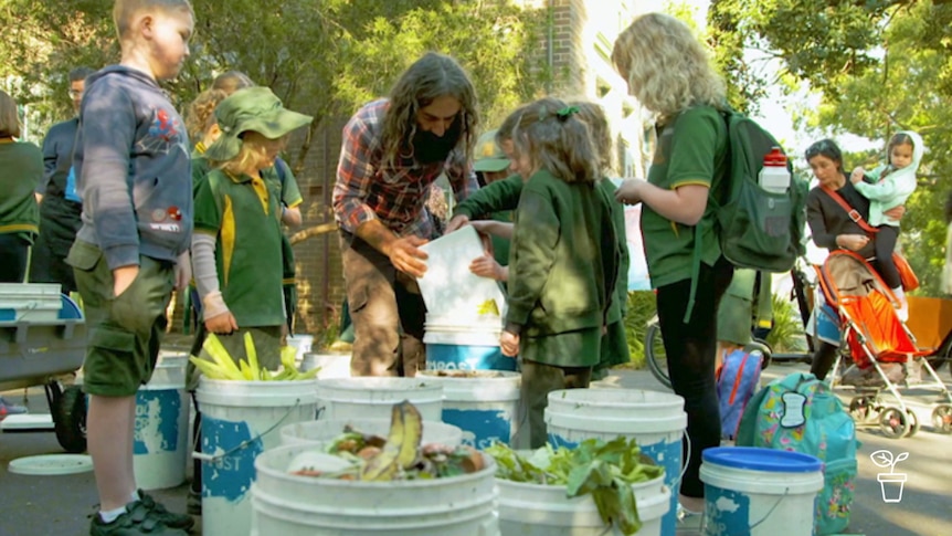 Man helping school children pour food scraps into buckets