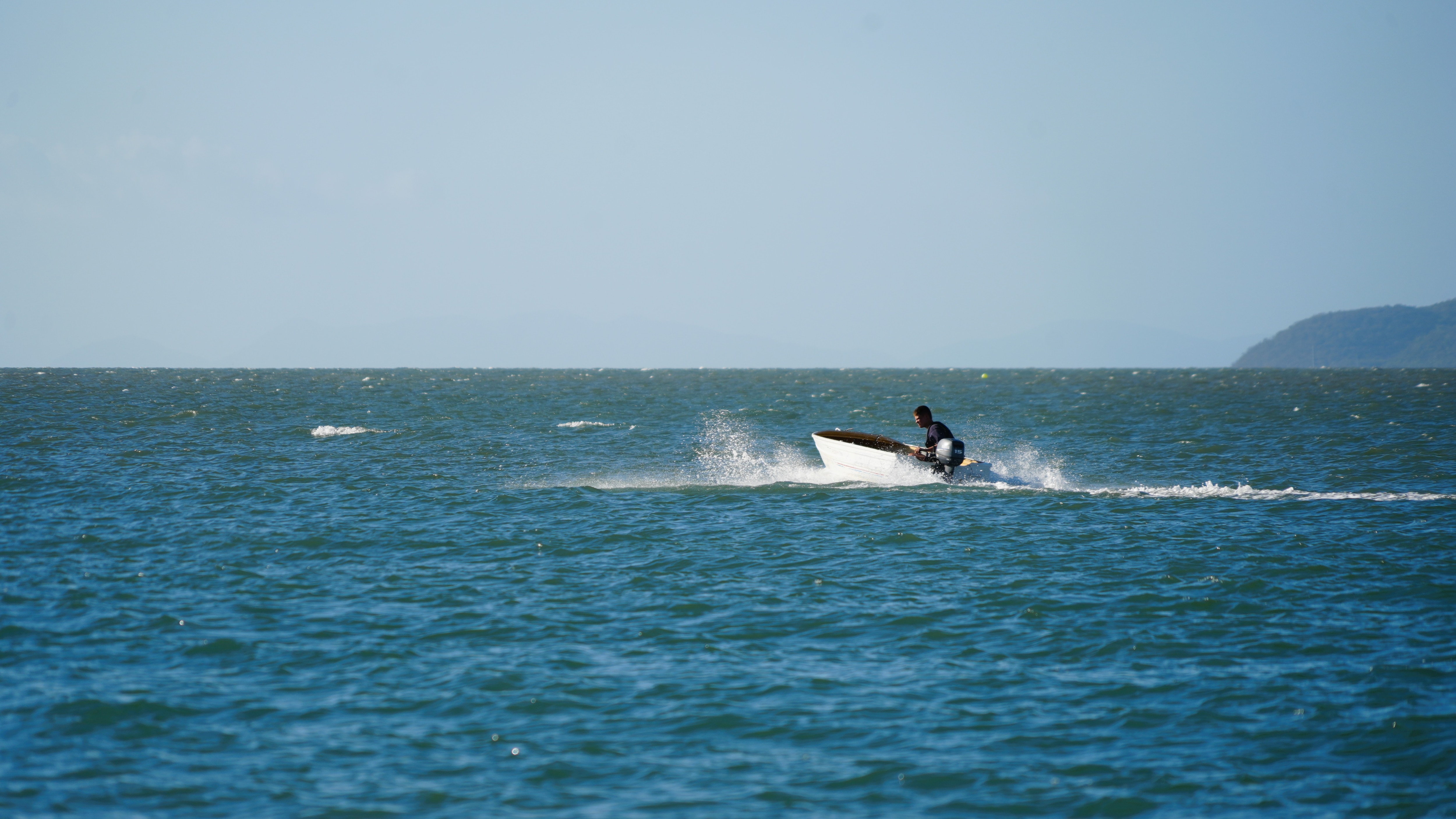 A man on a small boat in open water under clear skies.