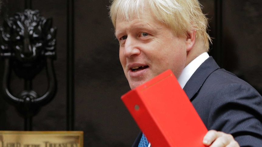 Boris Johnson holds a red folder and as he turns towards a door