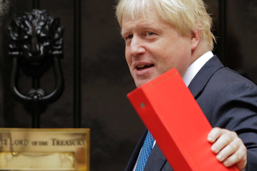 Boris Johnson holds a red folder and as he turns towards a door