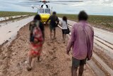 four people walk along a sodden dirt road towards a yellow liftflight helicopter